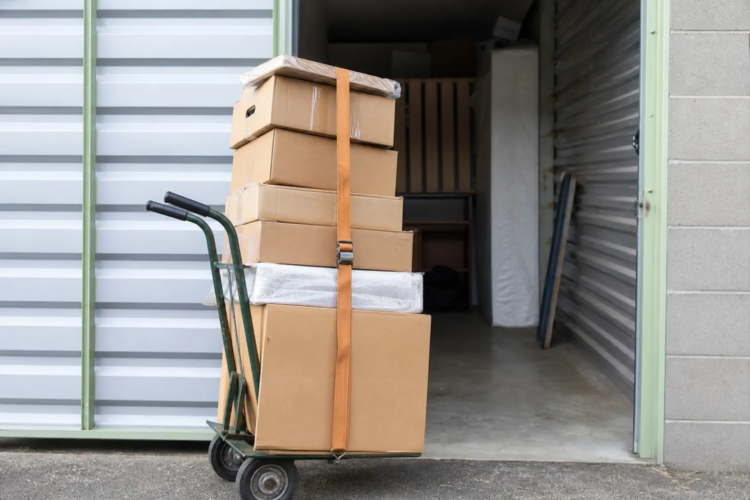 Diable de manutention chargé de cartons sanglés devant la porte ouverte d’un box de stockage